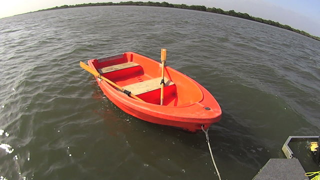 Orange colored dinghy tied to the back of a houseboat in full sun.
