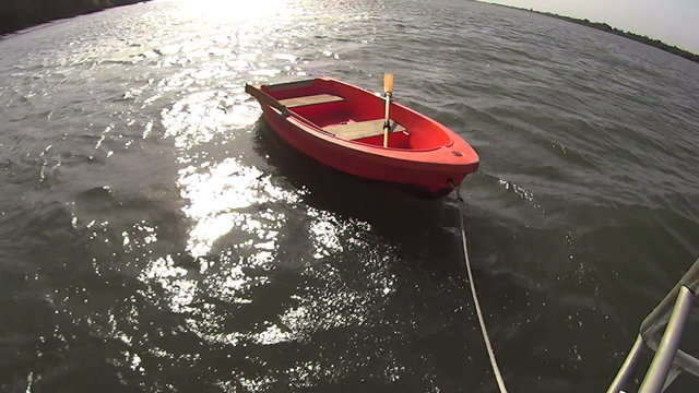Orange colored dinghy tied to the back of a houseboat with a sun reflection
