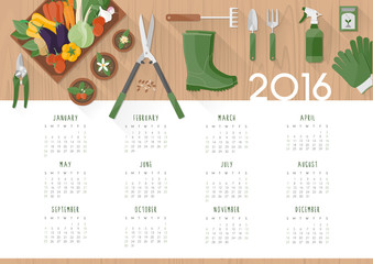 Gardening calendar 2016 with work tools, flower pots and vegetables in a crate on a  wooden table, top view