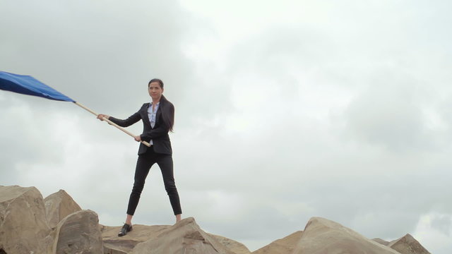 Young businesswoman waving a blue flag on mountain top 