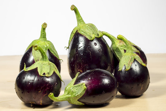 Several purple eggplants on wooden table and white background