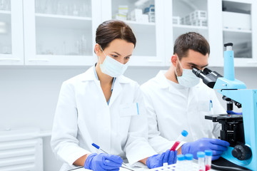 scientists with clipboard and microscope in lab