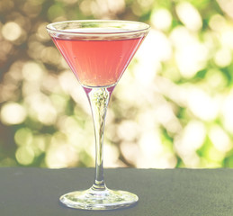 Cosmopolitan cocktail on a summer green nature bokeh background,