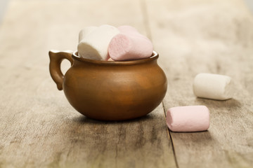 sweet marshmallows in a clay pot on wooden background