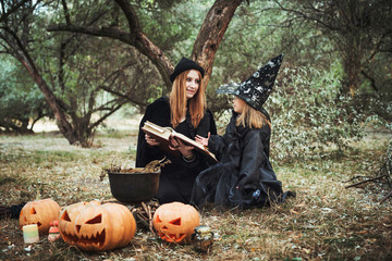 adult witch and small witch making magic in the wood. mother and daughter in halloween costumes