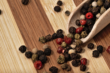 Grains of colored pepper on a wooden plank.