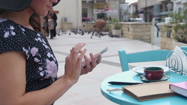 Female sitting at street cafe table, using smartphone, typing message, scrolling