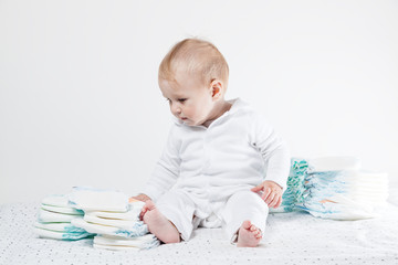 Baby sitzt auf dem Boden und schaut auf einen Stapel Windeln