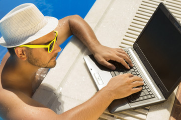 Young male working on laptop from a swimming pool 