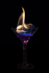 Martini glass with purple drink is on fire and very hot