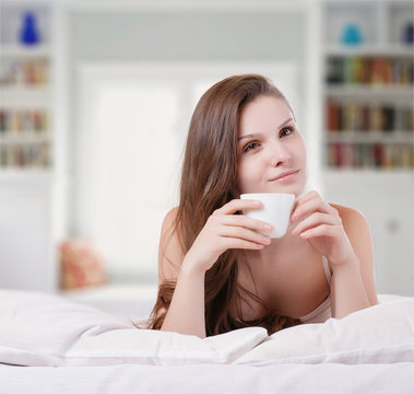 Woman on her bed smiling while holding a cup of coffee