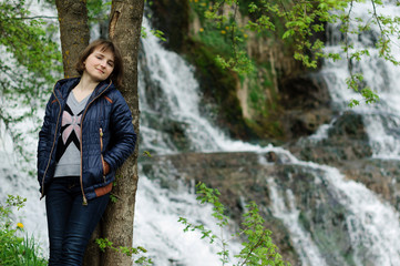 Young girl standing near forest waterfall. Dreaming