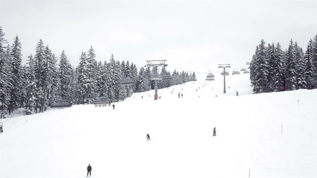 Various people skiing and snowboarding down a ski slope during a cloudy day. A ski lift is going up the mountain over the ski piste.