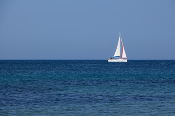 Fototapeta premium White yacht traveling with sails down on blue sea and sky horizon
