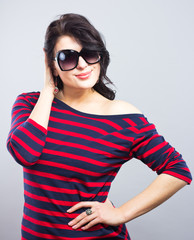 Beautiful brunette in a blue dress with red stripes. Fashion. Portrait of a young girl in sunglasses.
