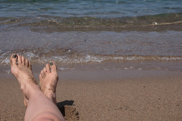 Wet female feet by water on sand
