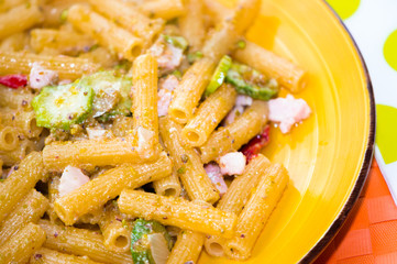 Pasta integrale con pesto al pistacchio, pancetta e zucchine, su tovaglietta arancione e piatto giallo