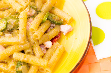 Pasta integrale con pesto al pistacchio, pancetta e zucchine, su tovaglietta arancione e piatto giallo