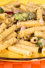 Pasta integrale con pesto al pistacchio, pancetta e zucchine, su tovaglietta arancione e piatto giallo