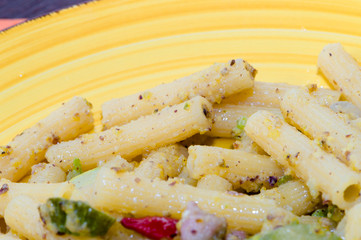 Pasta integrale con pesto al pistacchio, pancetta e zucchine, su piatto giallo