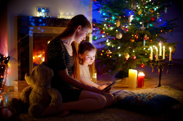 Naklejka premium Mother and daughter using a tablet by a fireplace on Christmas