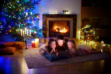 Obraz na płótnie Canvas Mother and daughters using a tablet by a fireplace on Christmas