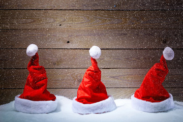 Fototapety  Santa kapelusze w śniegu z drewnianym tłem