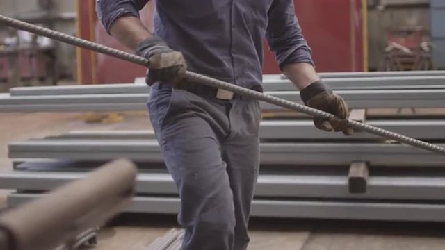 Steelworker carrying a length of rebar steel / metal to be pressed.