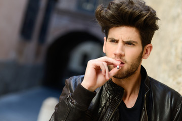 Young man smoking a cigarette in urban background