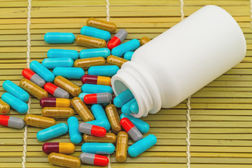 colorful pills and white bottle tablets on brown bamboo weave background