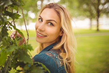 Portrait of cheerful woman standing by tree at park