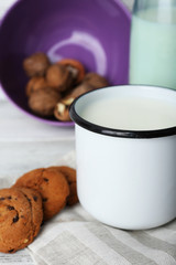 Milk in cup with walnuts and cookies on wooden table, closeup