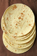 Stack of homemade whole wheat flour tortilla on brown napkin background