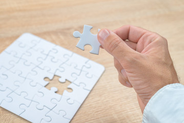 Businessman hand putting a missing piece into jigsaw puzzle