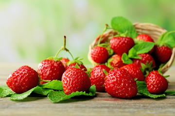 Ripe strawberries with leaves in wicker basket on wooden table on blurred background