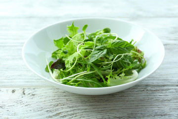 Fresh mixed green salad in bowl on wooden table close up