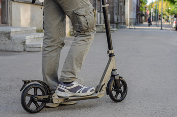 Obraz premium Young man in casual wear on kick scooter on street