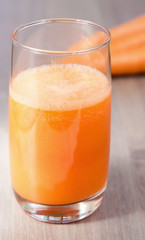 A glass of healthy carrot smoothie with carrots on wooden background