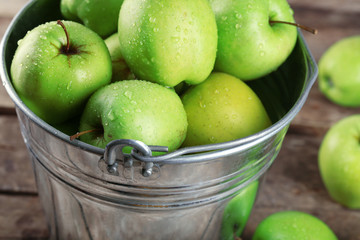 Ripe green apple in metal bucket on wooden table close up