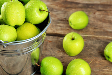 Ripe green apple in metal bucket on wooden table close up