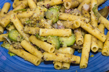 Pasta al pesto di pistacchi, con pancetta e zucchine. Tavola con piatto giallo, tagliere e cestino...