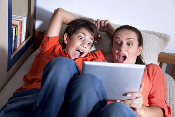 Surprised young boy and his mother are playing with tablet PC