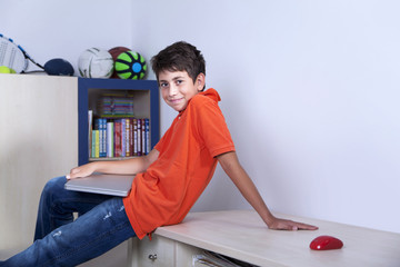 Happy young boy is sitting with his computer