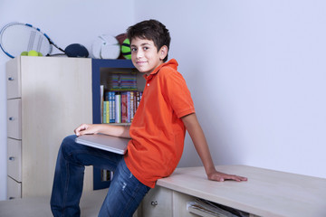 Happy young boy is sitting with his computer