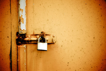 Rusty padlock on old orange painted wooden door