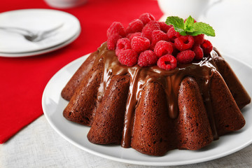 Tasty chocolate muffin with glaze and raspberries on table close up