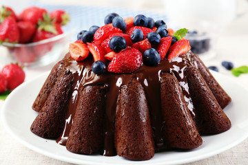 Tasty chocolate muffin with glaze and berries on table close up