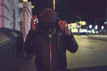 Urban afro man with woolen cap and headphones in city at night w