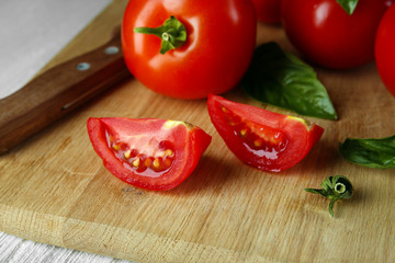 Whole and sliced red tomatoes on cutting board closeup