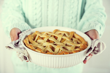 Homemade apple pie  in female hands, on light background